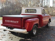 an old red and white pickup truck parked in a parking lot next to some trees