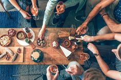 a group of people sitting around a wooden table with food and drinks on top of it