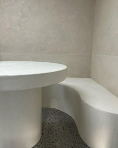 a white round table and bench in a room with tile flooring on the walls