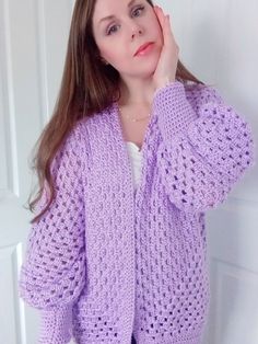 a woman wearing a purple cardigan standing in front of a white door with her hand on her face