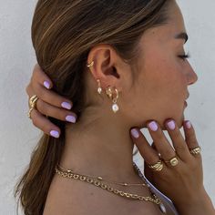 a woman with pink and gold nail polish holding her hand up to her ear while wearing two different rings