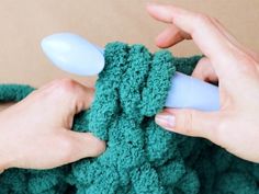 two hands are crocheting the ends of a green sweater