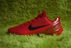 a pair of red nike shoes sitting on top of green grass in front of a wall