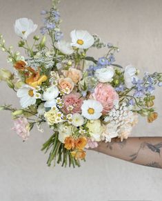 a woman holding a bouquet of flowers in her hand with tattoos on it's arm