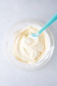 a bowl filled with whipped cream on top of a white counter next to a blue spoon