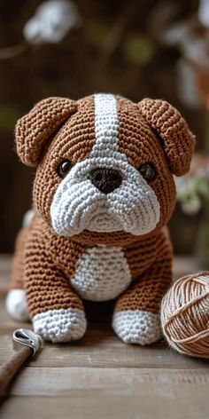 a brown and white knitted dog sitting next to a ball of yarn with a crochet hook