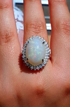 a woman's hand holding an opal and diamond ring