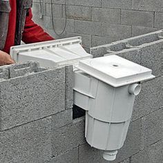 a man standing next to a brick wall with a white toilet attached to the side