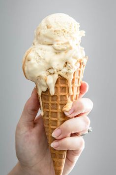 a hand holding an ice cream cone with white icing on it, in front of a gray background