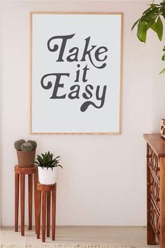 there is a plant and two potted plants in front of a poster that says take it easy