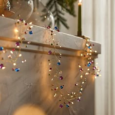 christmas lights are hanging on the wall next to a candle and some pine trees in the background