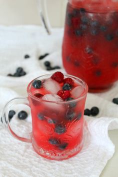 two glasses filled with berries and ice on top of a white towel next to a pitcher