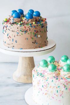 two cakes with sprinkles and chocolate frosting on each cake stand, one is white