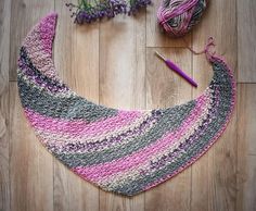 a crocheted pink, grey and white bib laying on top of a wooden floor