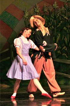 two women in dresses and hats are dancing on stage with one woman holding the other's hand