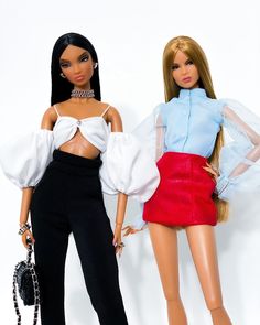 two barbie dolls standing next to each other on a white background with one holding a handbag