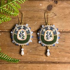 the earrings are decorated with beads and bead work on wood planks, surrounded by greenery