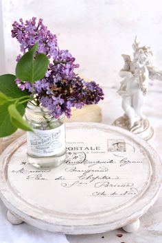 a vase with purple flowers sitting on top of a white table next to a small figurine