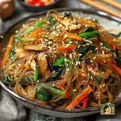 a plate full of noodles and vegetables with chopsticks