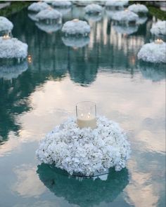 an arrangement of white flowers and candles in the middle of a pool filled with water