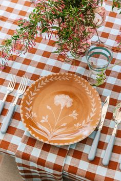 an orange and white plate sitting on top of a checkered table cloth next to silverware