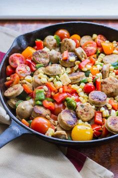 a skillet filled with corn, sausage and vegetables on top of a wooden table