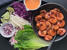 a plate with shrimp, lettuce and coleslaw next to dipping sauce