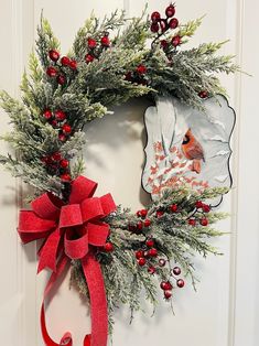 a christmas wreath hanging on a door with a red bow and cardinal ornament