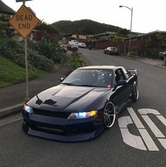 a black car parked on the side of a road next to a dead end sign