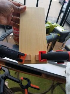 a person holding a piece of wood with pliers next to it on top of a table