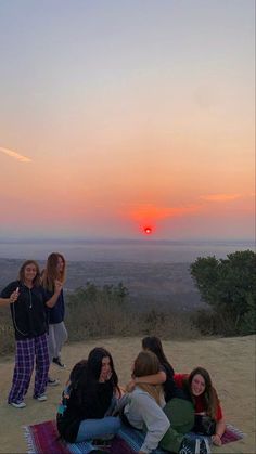 group of young people sitting on top of a hill watching the sun set in the distance