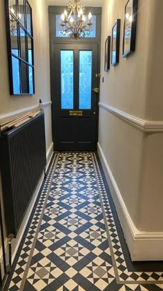 a hallway with black and white tile flooring and chandelier hanging from the ceiling