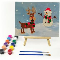 an easel with paint, markers and a painting of a snowman and reindeer