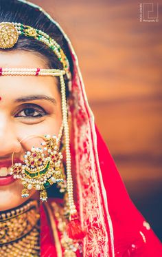 a woman wearing a red and gold bridal outfit with jewelry on her face, smiling at the camera