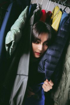 a woman is hiding in the closet with her coat on and looking at the camera