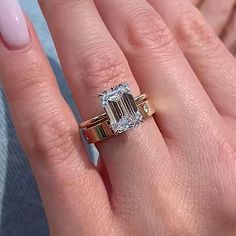 a woman's hand holding a ring with an emerald stone in the center and two gold bands around it