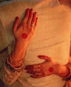 a woman with red nail polish holding her hands up to her chest and wearing gold bracelets