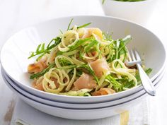 a white bowl filled with pasta and veggies on top of a table next to a fork