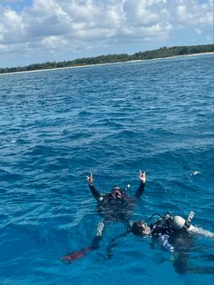 two people floating in the ocean with their hands up and one person wearing scuba gear