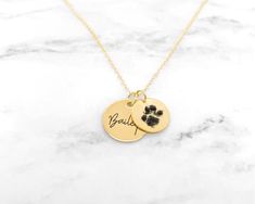 a gold necklace with a paw print on it and the word beauly written in black ink