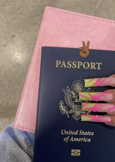 a person with pink and yellow nail polish holds up a passport in front of them