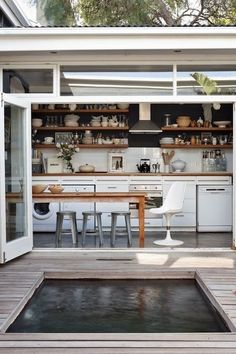 an outdoor kitchen with white cabinets and wooden flooring is seen from the outside area