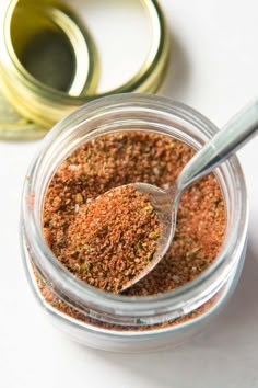 an open jar filled with spices next to a container of seasoning and a spoon