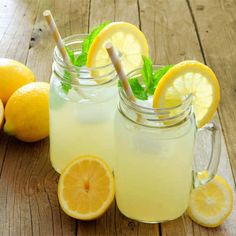 two mason jars filled with lemonade sitting on top of a wooden table next to sliced lemons