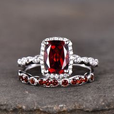 a red and white diamond ring set on top of a stone slab with garnets around it