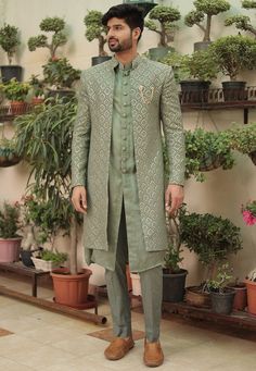 a man standing in front of potted plants wearing a green sherve coat