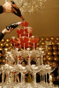 a person pouring champagne into wine glasses on top of a table filled with gold and red balloons