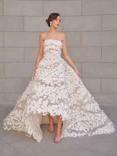 a woman standing in front of a wall wearing a white dress with flowers on it