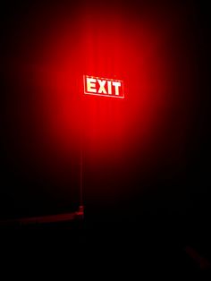 an exit sign lit up in the dark with red light shining on it's side