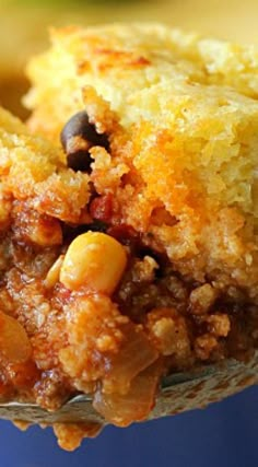 a close up of a piece of food on a spoon with cornbread and beans